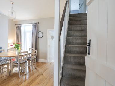 A dining area with a wooden table and chairs next to a staircase with carpet at Cobblers Cottage in Beaumaris
