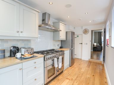 A kitchen with white cabinets wooden countertops stainless steel stove and refrigerator at Cobblers Cottage in Beaumaris