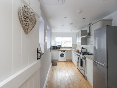A kitchen with wooden floor cabinets a refrigerator stove microwave and washing machine at Cobblers Cottage Beaumaris