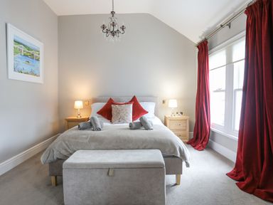 A bedroom with a double bed two bedside tables with lamps a bench at the foot of the bed and red curtains at Cobblers Cottage in Beaumaris