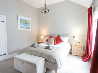 A bedroom with a bed with red pillows bedside tables lamps a chandelier and a window with red curtains at Cobblers Cottage in Beaumaris