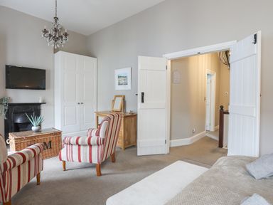 A sitting room with striped armchairs a wardrobe and a wall mounted television at Cobblers Cottage in Beaumaris