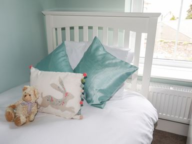 A bed with two teal pillows a decorative pillow with a rabbit design and a teddy bear near a window at Cobblers Cottage in Beaumaris