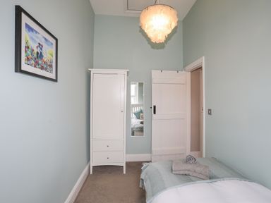 A bedroom with a bed covered with folded towels a white wardrobe a wall mirror an open door and a ceiling light at Cobblers Cottage in Beaumaris