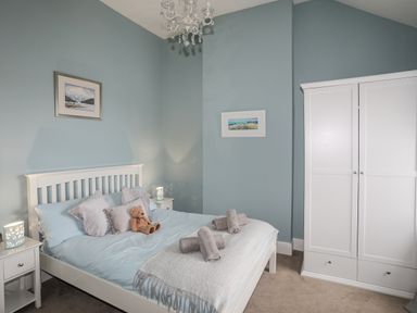 A bedroom with a bed with pillows and a teddy on it beside two nightstands with lamps and a white wardrobe at Cobblers Cottage Beaumaris
