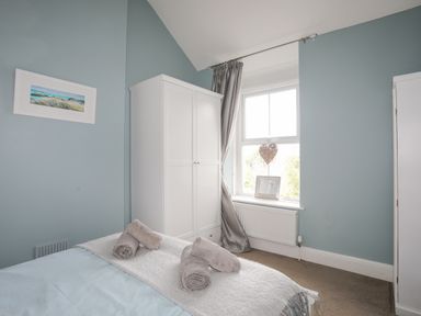 A bedroom with a bed with rolled towels beside a white wardrobe and a window with a heart decoration at Cobblers Cottage in Beaumaris