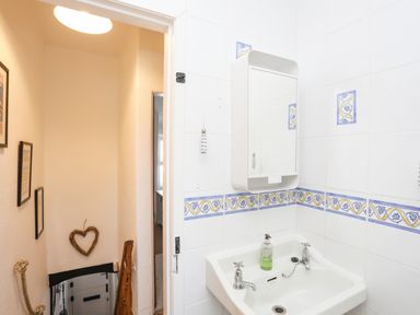 A small bathroom with a white sink and wall mirror next to a staircase with framed pictures and a heart decoration at Menuchah in Criccieth