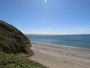 A view of a beach with sand and pebbles next to a cliff and the sea at Menuchah in Criccieth