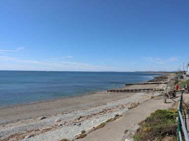 A pebble beach with wooden groynes and a paved walkway along the coast at Menuchah in Criccieth