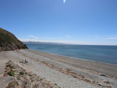 A rocky beach with a few people sitting and walking near the shoreline with hills in the distance at Menuchah in Criccieth