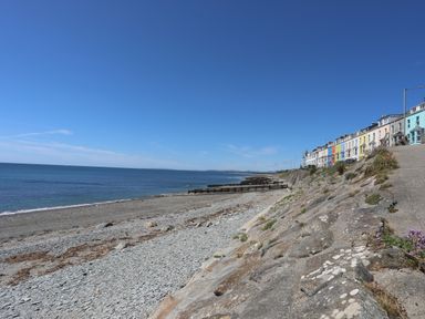 A pebble beach with a stone seawall and colorful houses on the right at Menuchah in Criccieth