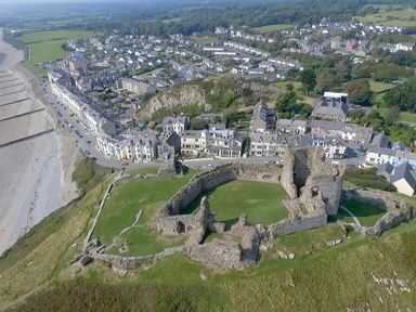 An aerial view of castle ruins near a coastal town with houses and fields in Criccieth