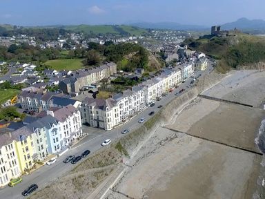 A coastal town with a row of houses along a road by a beach and a castle on a hill at Menuchah in Criccieth