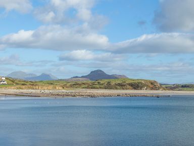 A coastal landscape with a beach and hills under a partly cloudy sky at Menuchah in Criccieth
