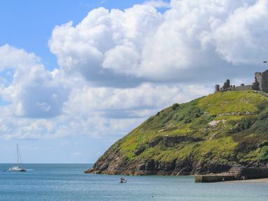 A coastal hillside with castle ruins and boats on the water at Menuchah in Criccieth