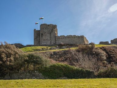 A stone castle on a hill with two Welsh flags flying at Menuchah in Criccieth
