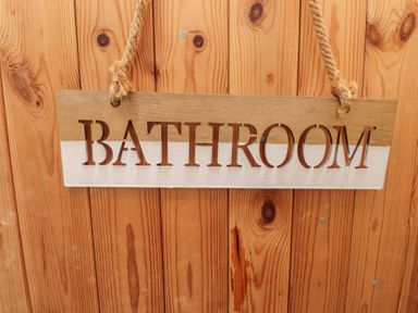 A bathroom sign made of wood hanging on a wall at Menuchah in Criccieth