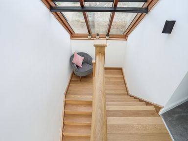 A wooden staircase with a gray chair and pink pillow under a skylight window at The Stables in Penmon near Beaumaris