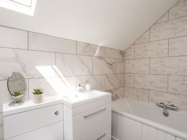 A bathroom with a white sink and cabinet a small round mirror a potted plant and a bathtub at The Stables in Penmon near Beaumaris