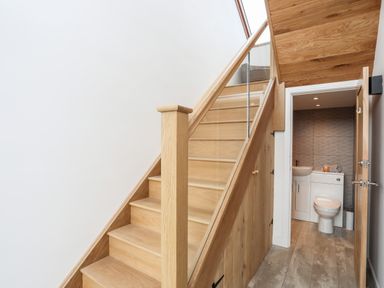 A staircase with wooden steps and glass panels next to a small bathroom with a toilet and sink at The Stables in Penmon near Beaumaris
