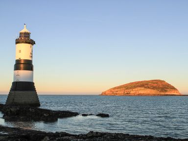 A lighthouse on a rocky shore with an island in the sea at The Stables in Penmon near Beaumaris