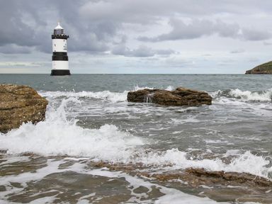 A seascape with a lighthouse in the distance waves crashing on rocks near the shore at The Stables in Penmon near Beaumaris