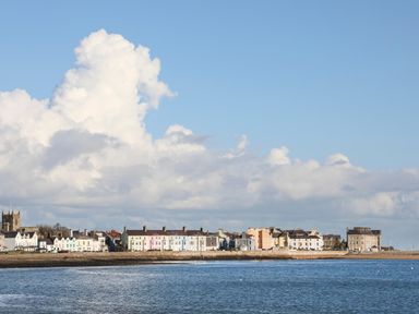 A coastal town with a row of houses and a church near the water at The Stables in Penmon near Beaumaris