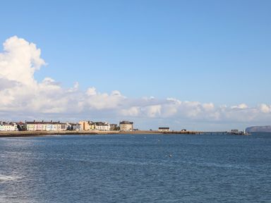 A coastal town with buildings along the shore and a pier extending into the sea with a blue sky above at The Stables in Penmon near Beaumaris