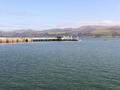 A pier extending into calm water with hills in the background at The Stables in Penmon near Beaumaris