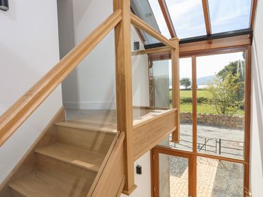 A wooden staircase with glass panels next to large windows showing an outdoor view at The Stables in Penmon near Beaumaris