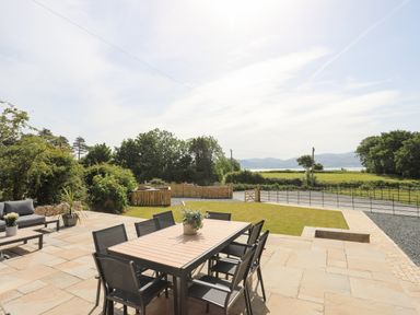 An outdoor patio with a dining table and chairs a seating area a lawn and countryside views at The Stables in Penmon near Beaumaris