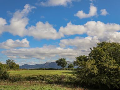 A field with trees and mountains in the background under a partly cloudy sky at The Stables in Penmon near Beaumaris