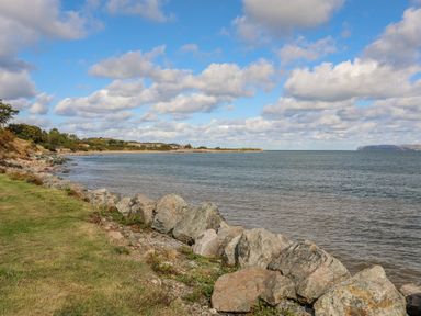 A rocky shoreline with grass and water under a partly cloudy sky at The Stables in Penmon near Beaumaris