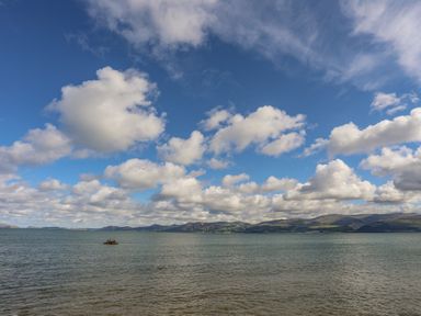 A body of water with a small rocky island and mountains in the background under a sky with scattered clouds at The Stables in Penmon near Beaumaris
