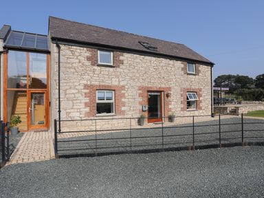 An exterior view of a stone and brick house with a small black fence and a gravel driveway at The Stables in Penmon near Beaumaris