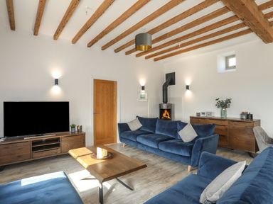 A living room with blue sofas wooden furniture a wood burning stove and exposed ceiling beams at The Stables in Penmon near Beaumaris