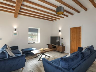 A living room with blue sofas wooden coffee table TV and exposed wooden ceiling beams at The Stables in Penmon near Beaumaris