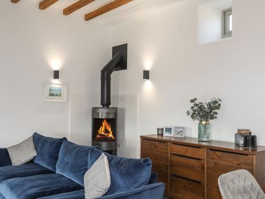 A living room with a blue sofa a wooden dresser a small window and a fireplace at The Stables in Penmon near Beaumaris