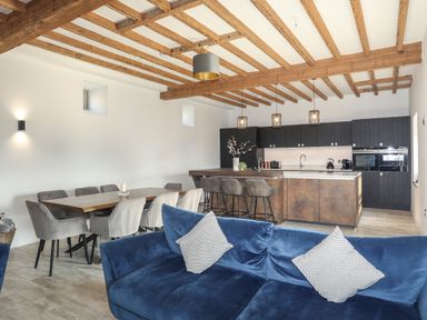An open-plan room with a blue sofa, a dining table with chairs, and a kitchen with island and bar stools at The Stables in Penmon near Beaumaris
