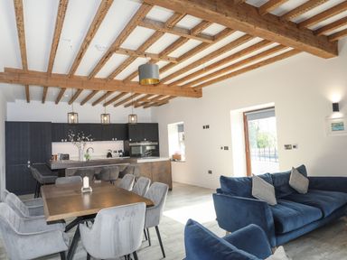 An open-plan kitchen dining and living area with wooden ceiling beams and grey and blue furniture at The Stables in Penmon near Beaumaris