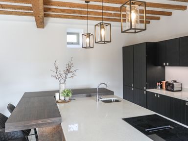 A kitchen with a white countertop island a stove and black cabinets at The Stables in Penmon near Beaumaris