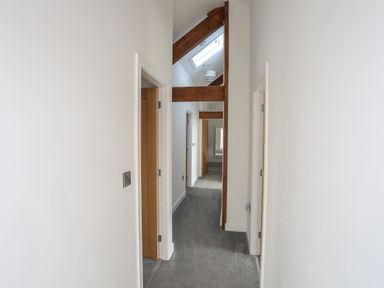 A hallway with carpet flooring wooden beams and open doors leading to other rooms at The Stables in Penmon near Beaumaris