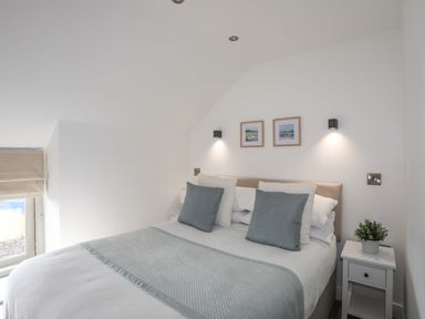 A bedroom with a bed with blue and white pillows and a blue throw with two picture frames on the wall and a bedside table with a plant at The Stables in Penmon near Beaumaris