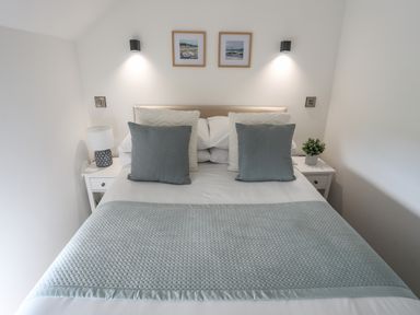 A bedroom with a double bed grey cushions white bedside tables a lamp and a plant at The Stables in Penmon near Beaumaris
