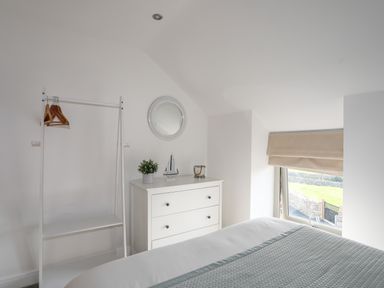A bedroom with a chest of drawers a clothes rack with hangers a bed and a window at The Stables in Penmon near Beaumaris