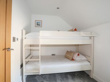 A bedroom with a white bunk bed and pillows on each bed at The Stables in Penmon near Beaumaris