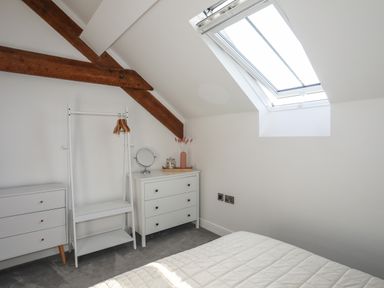 A bedroom with white furniture wooden beams skylight and a bed at The Stables in Penmon near Beaumaris