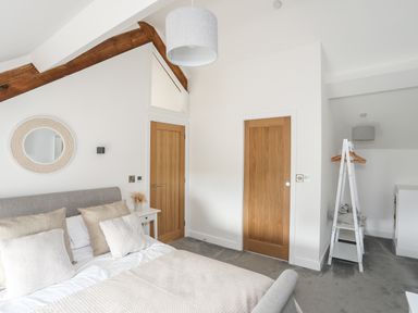 A bedroom with a bed with pillows a bedside table with dried flowers a round mirror two wooden doors and a white clothes stand at The Stables in Penmon near Beaumaris