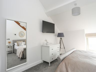 A bedroom with a bed a chest of drawers a floor lamp a wall-mounted TV and a mirror reflecting another bed at The Stables in Penmon near Beaumaris