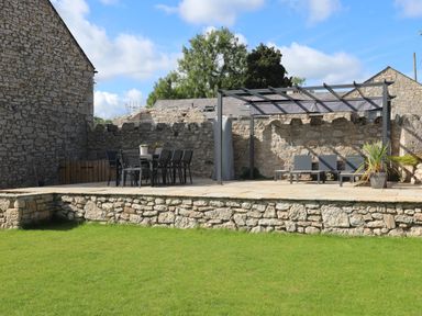 An outdoor patio with a dining table and chairs next to a pergola with lounge chairs and a potted plant at The Stables in Penmon near Beaumaris